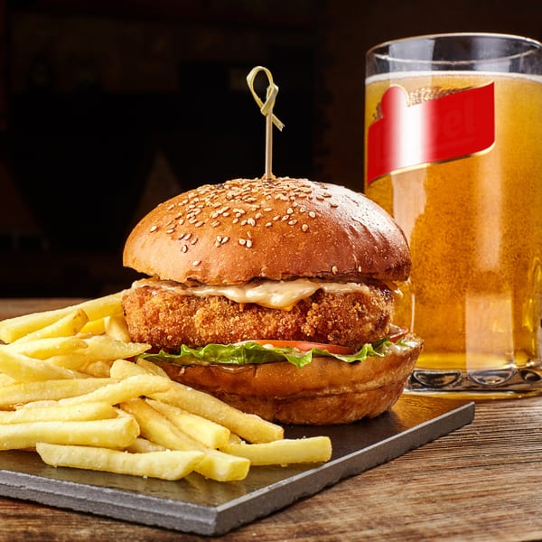 Crispy chicken burger with fries and a glass of beer on a wooden table.
