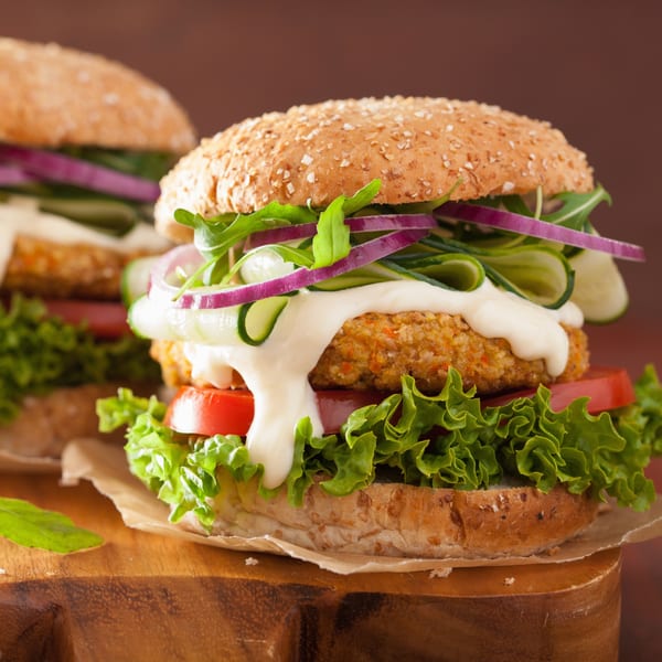 Two vegan burgers with lettuce, tomato, cucumber, red onion, arugula, and white sauce.
