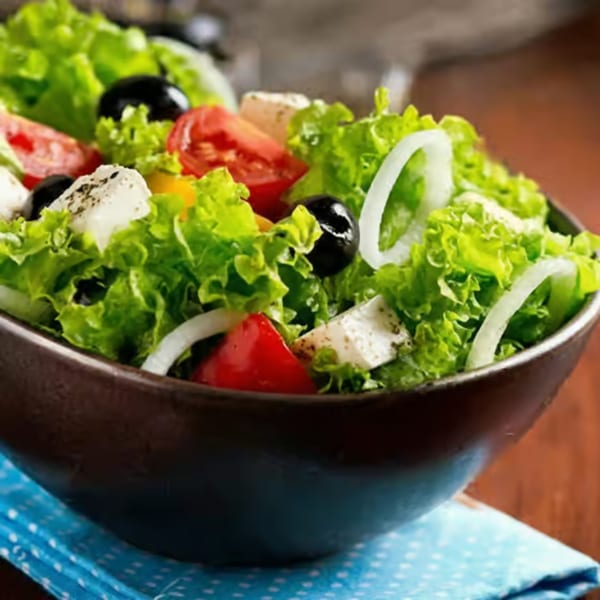 A fresh garden salad with lettuce, tomatoes, onions, olives, and feta cheese in a dark bowl.