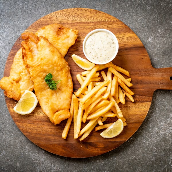 Golden-brown fish and chips with tartar sauce and lemon wedges on a wooden board.